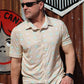 A man exudes cool confidence in HowdyHo's Sunrise Serenity shirt, a perfect blend of casual elegance and comfort. The shirt's soft tan color with a light green and white floral pattern provides a fresh and relaxed look. Accessorized with sleek sunglasses and paired with classic denim jeans, this ensemble is set against a colorful, rustic urban background, showcasing the shirt's versatility for any laid-back occasion.